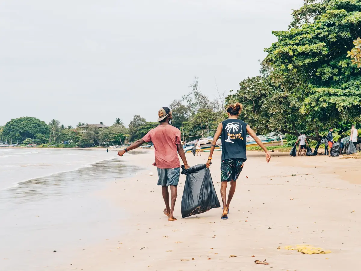 Volunteers carrying a bag of collected trash along a beach shoreline